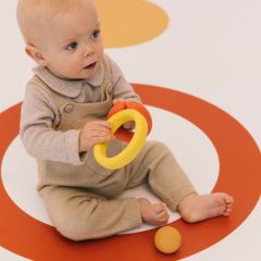 Niemowlę bawiące się żółtym sensorycznym gryzakiem w kształcie kapsuły na kolorowej macie. Oli & Carol Naturalna Zabawka Sensoryczna 4w1 Evolutive Capsule