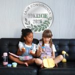 Dwie dziewczynki siedzące na czarnej kanapie z bidonami termicznymi i pojemnikami na przekąski dla dzieci. b.box Butelka termiczna 690ml Sea Glass