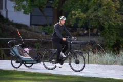 Kobieta jadąca na rowerze z przyczepką rowerową dla dziecka na tle zieleni