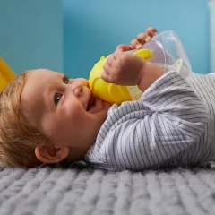 Niemowlę leżące na plecach pijące wodę z butelki z żółtym ustnikiem