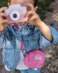 Różowy aparat dla dzieci z torbą na ramię, trzymany przez dziecko w jeansowej kurtce. Hoppstar Expert Blush Zestaw aparat dla dzieci i torba na aparat