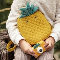 Żółty aparat dla dzieci w kształcie ananasa z zielonymi liśćmi i dopasowana torba w dłoni dziecka. Hoppstar Rookie Pina Coolada Zestaw aparat dla dzieci i torba