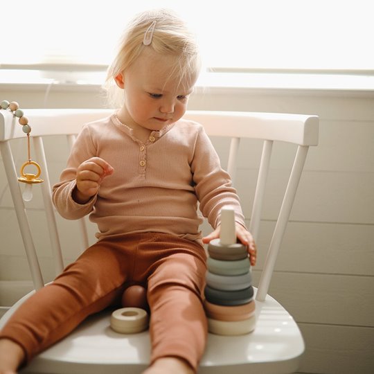Dziecko bawi się sensoryczną piramidką z kolorowych kółek na krzesełku. Mushie Piramidka sensoryczna kółka Orginal
