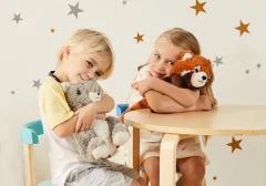 Dwoje dzieci siedzi przy stoliku i trzyma pluszowe maskotki w pokoju z gwiazdkami na ścianie