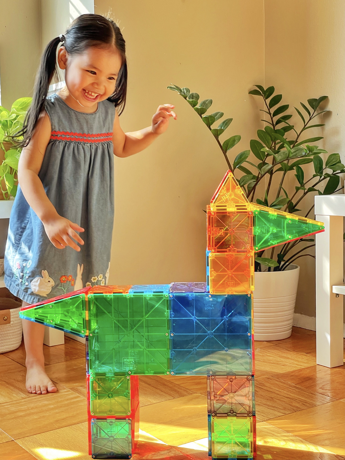 Dziecko bawi się kolorowymi klockami magnetycznymi tworząc wieżę i konstrukcję na podłodze. Magna-Tiles Klocki Magnetyczne Classic 100el