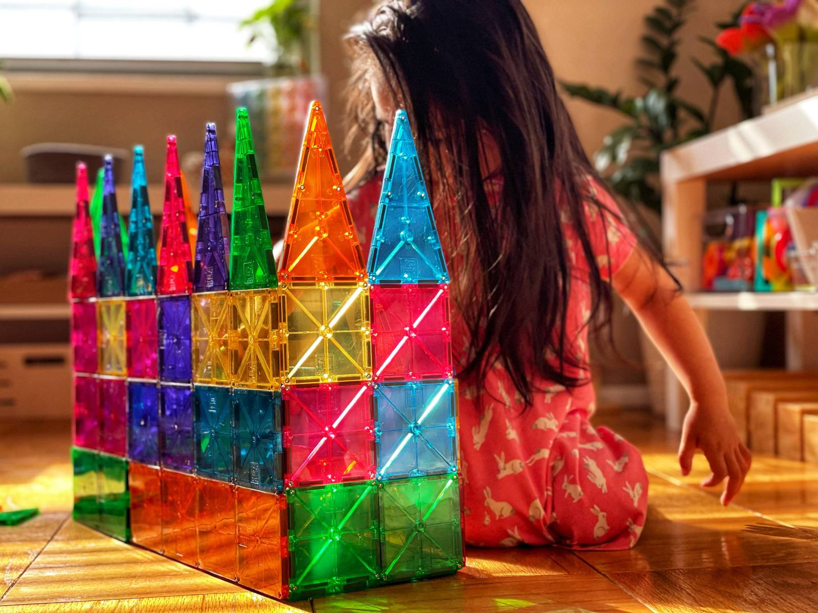 Dziecko bawi się kolorowymi magnetycznymi klockami w kształcie kwadratów i trójkątów tworząc wieżę i ścianę. Magna-Tiles Klocki Magnetyczne Classic 100el