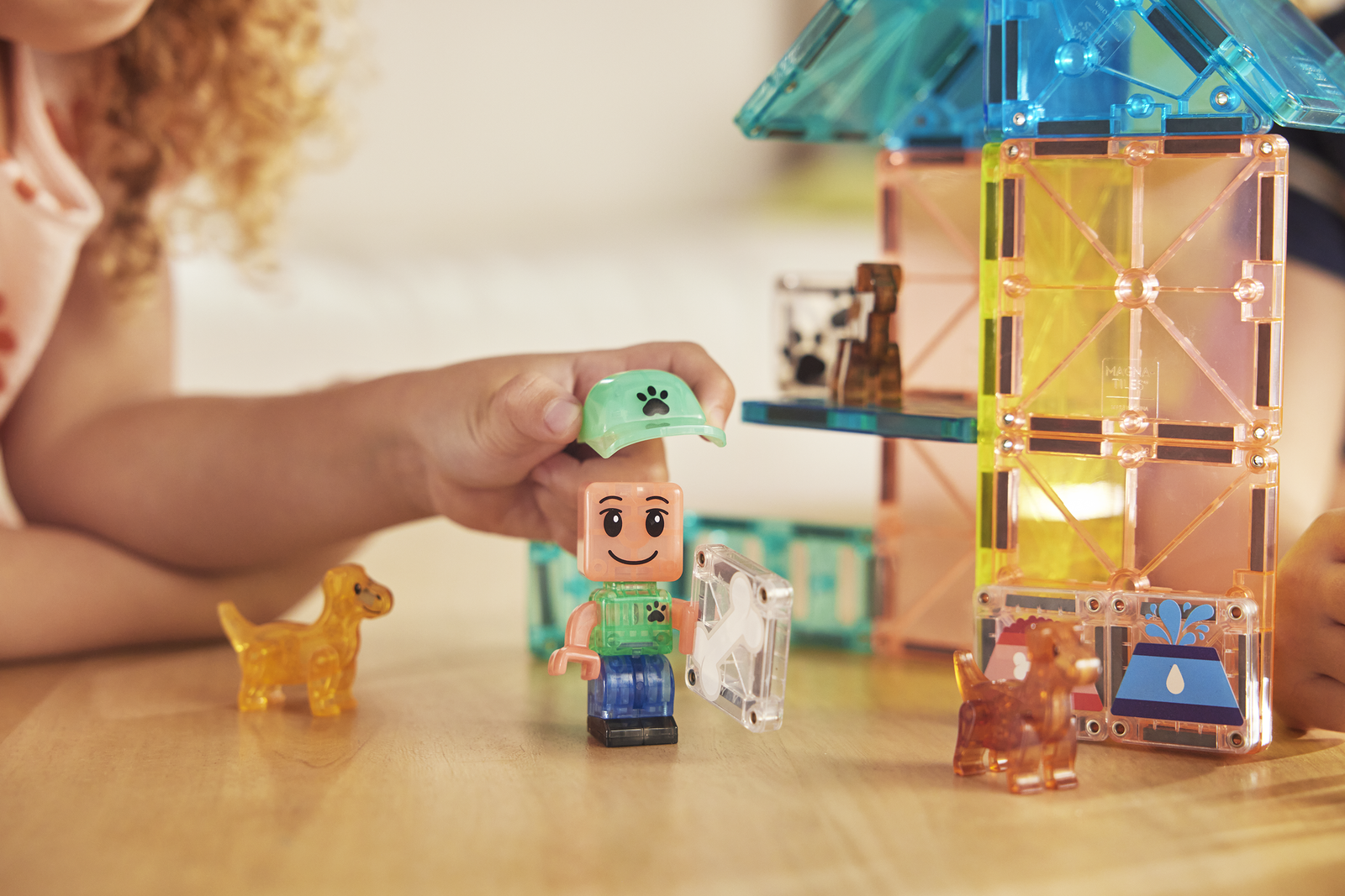 Dziecko bawi się magnetycznymi klockami z figurką i dwoma pieskami przy kolorowej konstrukcji. Magna-Tiles Klocki Magnetyczne Puppy Park 27el