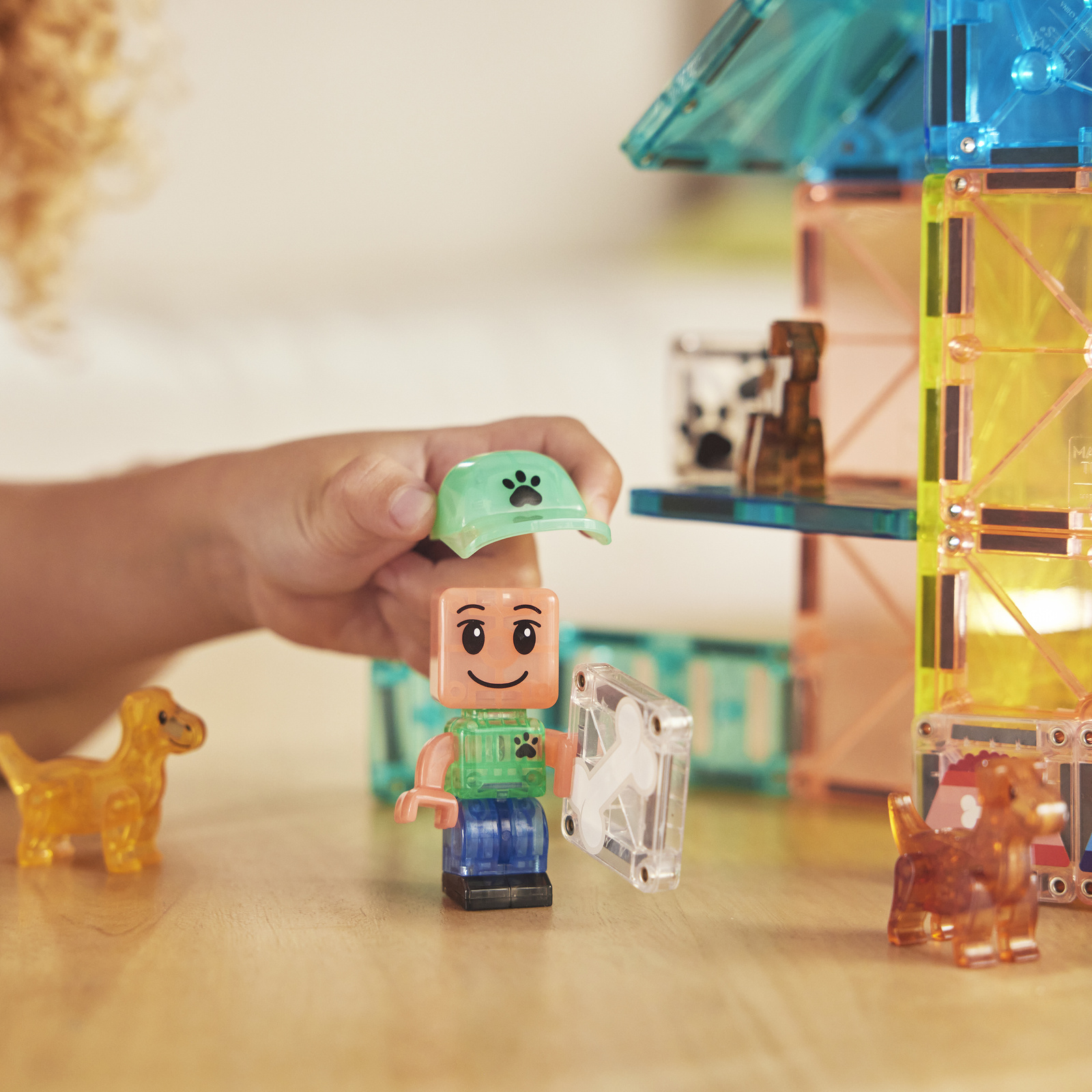 Dziecko trzyma figurkę z zielonym kapeluszem przy magnetycznych klockach i małych pieskach. Magna-Tiles Klocki Magnetyczne Puppy Park 27el