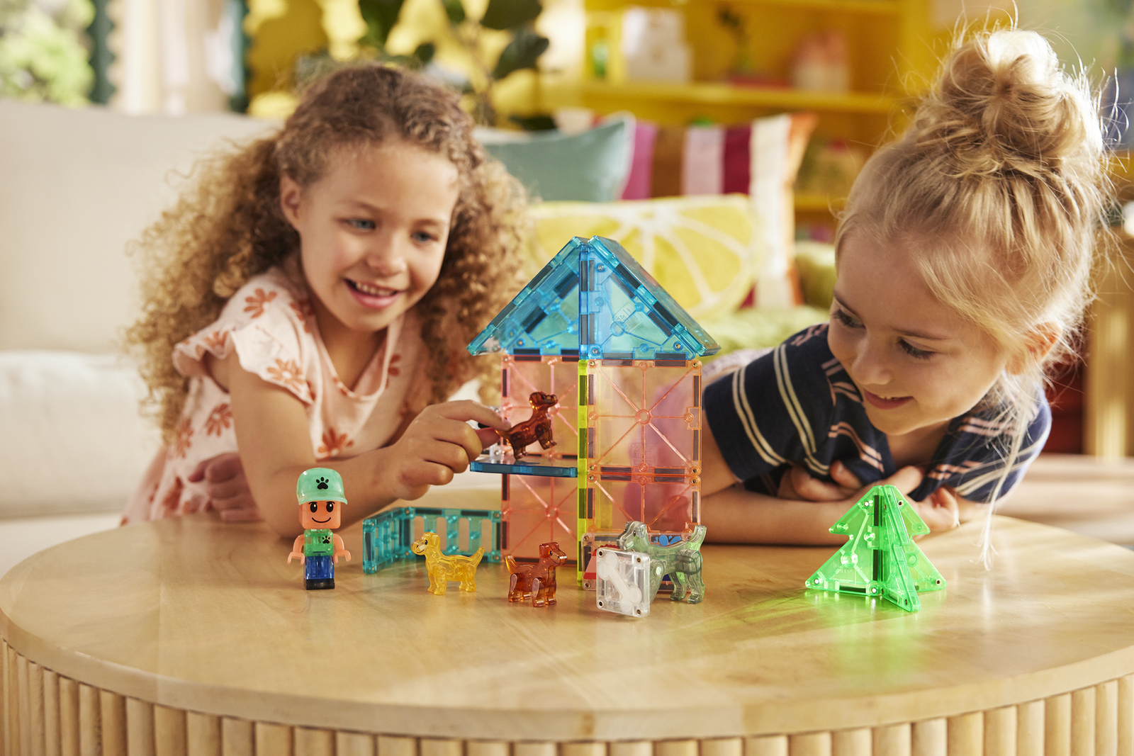 Dzieci bawiące się magnetycznymi klockami zbudowanymi w kolorowy domek i figurkami psa oraz postaci. Magna-Tiles Klocki Magnetyczne Puppy Park 27el