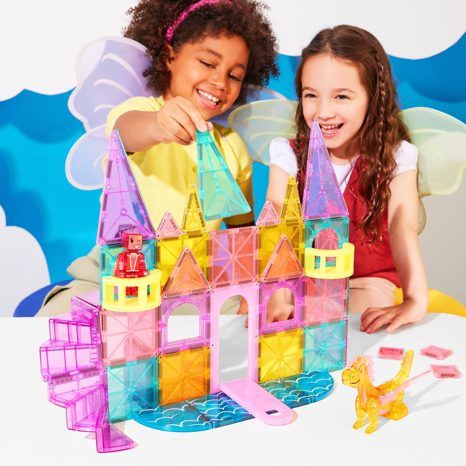 Dzieci budują kolorowy zamek z magnetycznych klocków z wieżyczkami i mostem. Magna-Tiles Klocki Magnetyczne Zamek DLX 48el