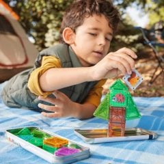 Dziecko bawi się magnetycznymi klockami tworząc wieżę i zielony domek na stole piknikowym. Magna-Tiles Klocki Magnetyczne microMAGS Treehouse Travel 24el