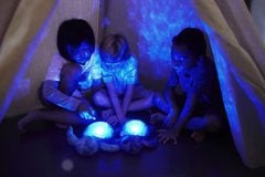 Dzieci oglądają świecący projektor w kształcie żółwia pod namiotem z koców. Cloud B Projektor z pozytywką Żółw podwodny różowy ECO Tranquil Turtle