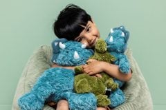 Zielony pluszowy triceratops przytulany przez dziecko na tle dużych niebieskich maskotek dinozaurów