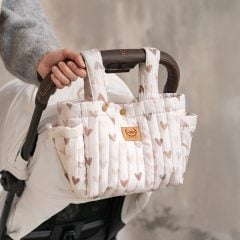 Pikowany organizer do wózka w jasnym kolorze z wzorem różowych i brązowych serc, zawieszony na rączce wózka