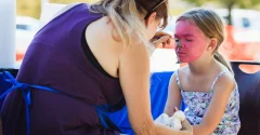 Malowanie twarzy dziecka różową farbą przy użyciu pędzelka przez dorosłą osobę