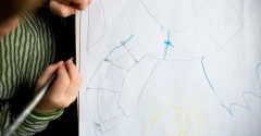 Dziecko rysujące kredką na dużej kartce papieru widocznej z kolorowymi liniami i kształtami