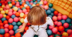 Dziecko siedzi w basenie z kolorowymi piłeczkami i dotyka ich rękami