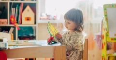 Dziecko siedzące przy stoliku wycina papier nożyczkami, trzymając kolorowy arkusz z wzorem geometrycznym