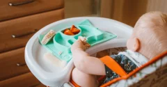 Niemowlę w krzesełku do karmienia z tacką i silikonową podkładką z przegródkami na pieczywo i warzywa