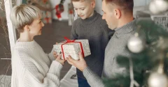 Rodzina trzymająca wspólnie świąteczny prezent przy choince
