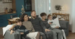 Rodzina ogląda świąteczny film na kanapie, chłopiec trzyma pilota, w tle choinka i dekoracje świetlne