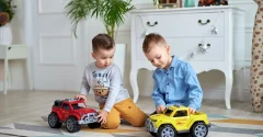 Dwóch chłopców bawi się obok siebie czerwonym i żółtym samochodem zabawkowym na podłodze